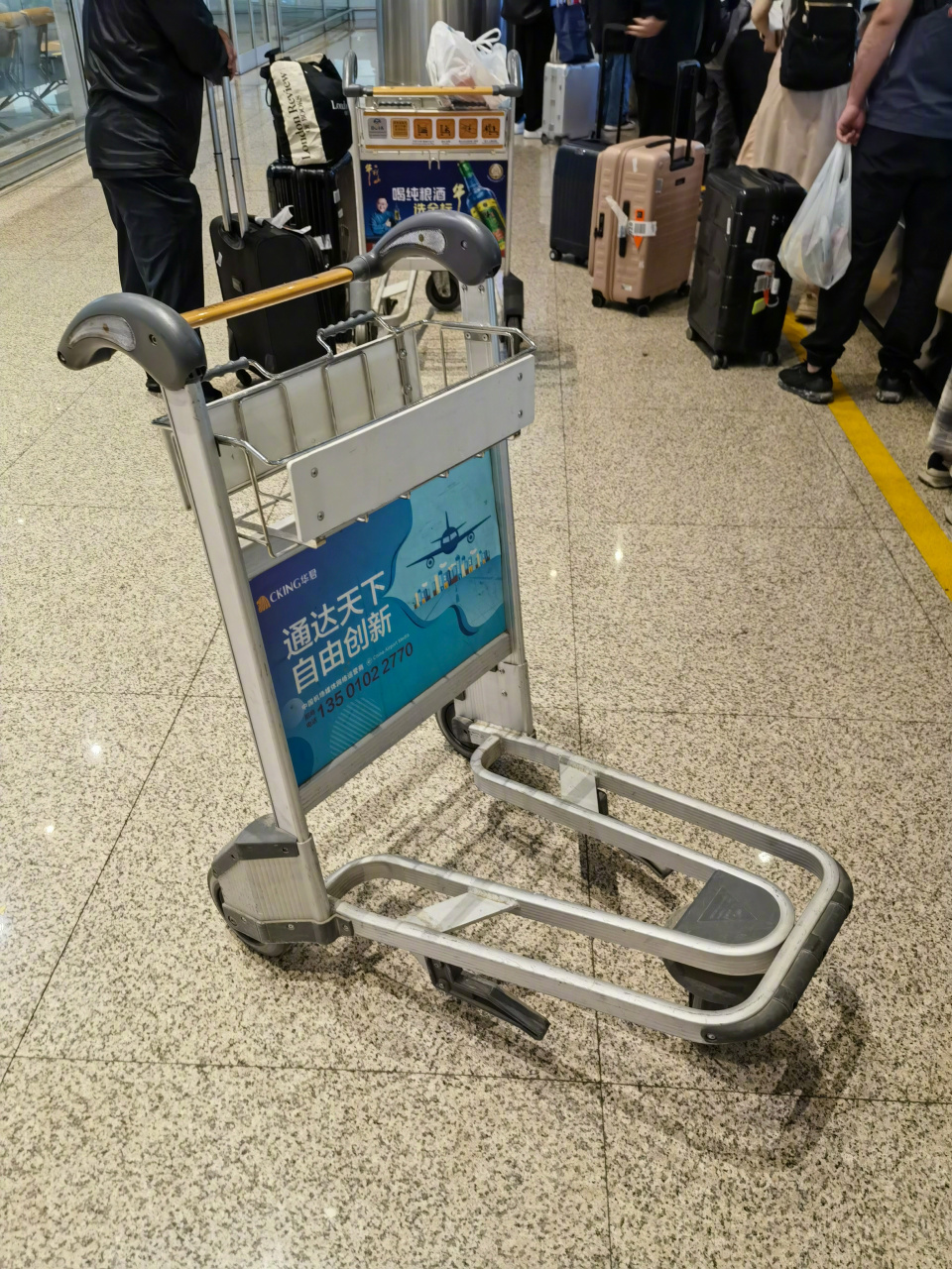 4岁小朋友侧坐在行李车右侧,她妈妈推着车,小朋友脚