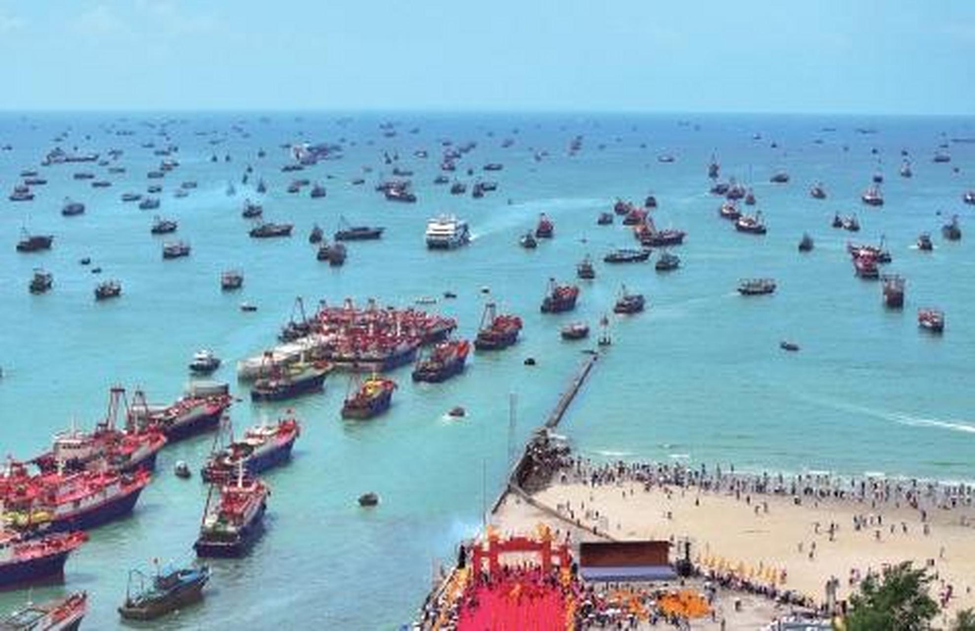 8月16日,游人在广西北海市侨港镇电建渔港码头的出海口观赏渔船出港的