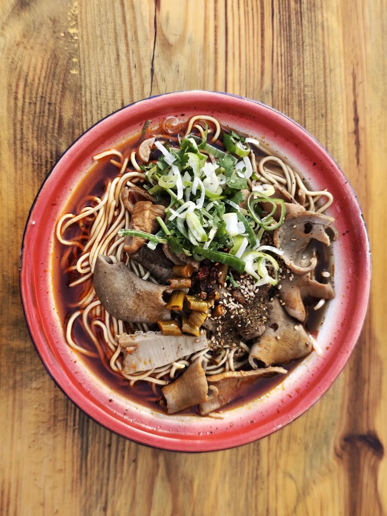 做法很讲究,半篓碱面和豆芽烫熟,加牛骨汤,再放滚烫的牛肉或牛杂,撒上