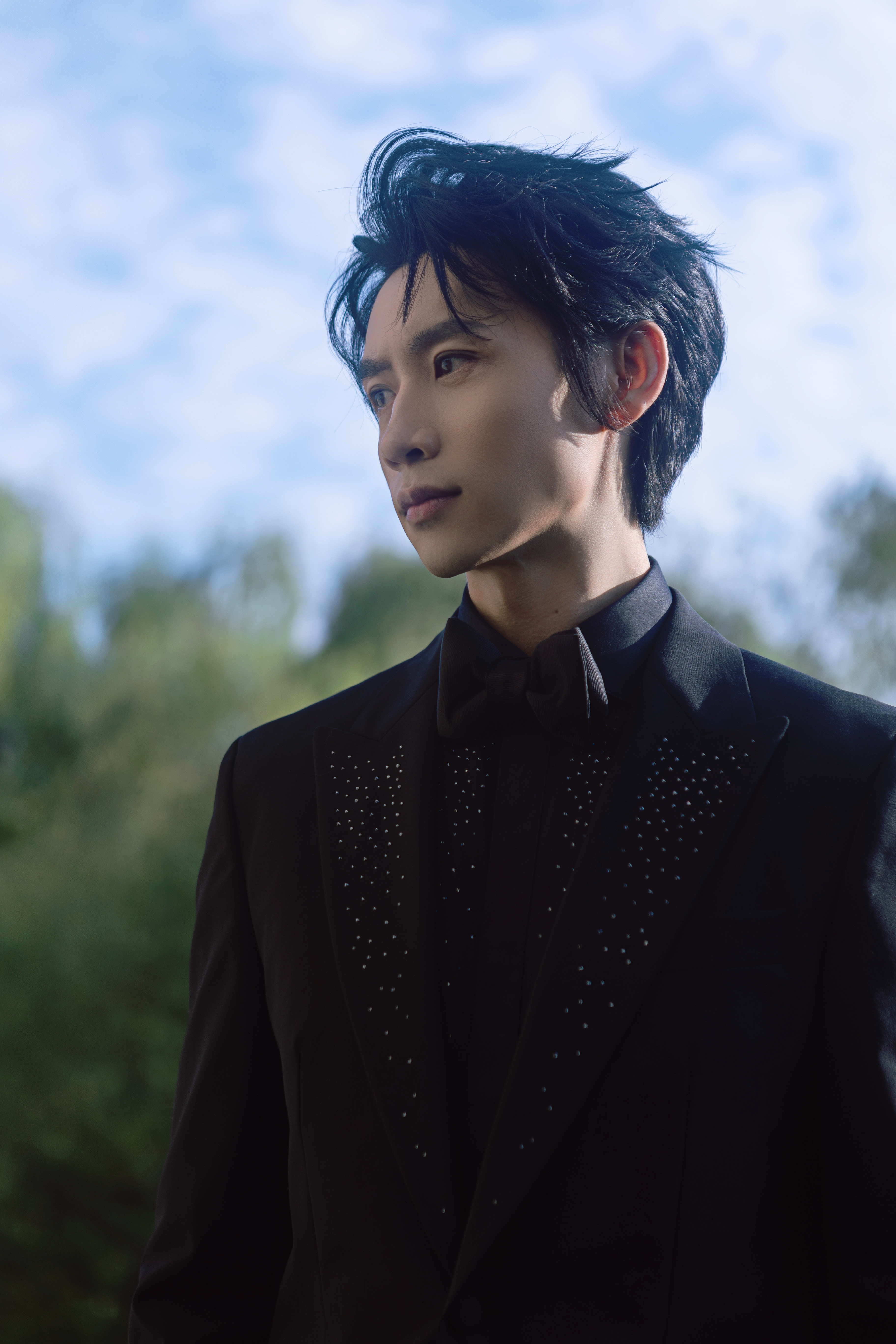 眼眸澄澈清隽,黑色西装内敛沉稳,与葱郁之景相映,携热爱前行,赴约光影