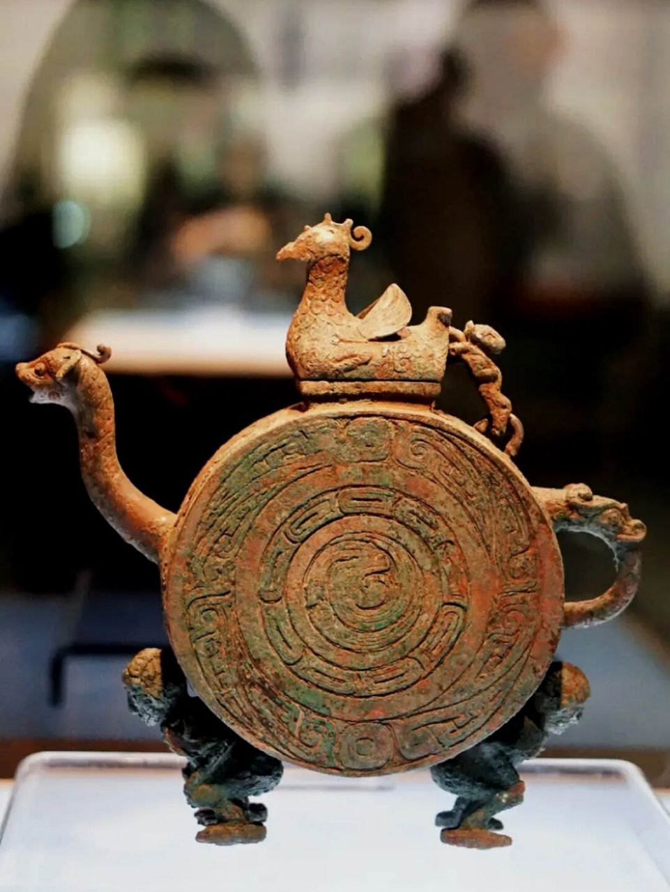 器体扁圆,顶有长方形口,上有圆雕的振翅鸟形盖