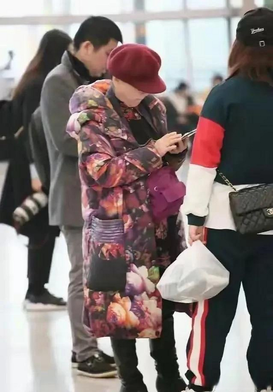 李谷一现身机场,身着花棉衣,脚穿长筒高跟靴,头戴紫色帽,精神抖擞