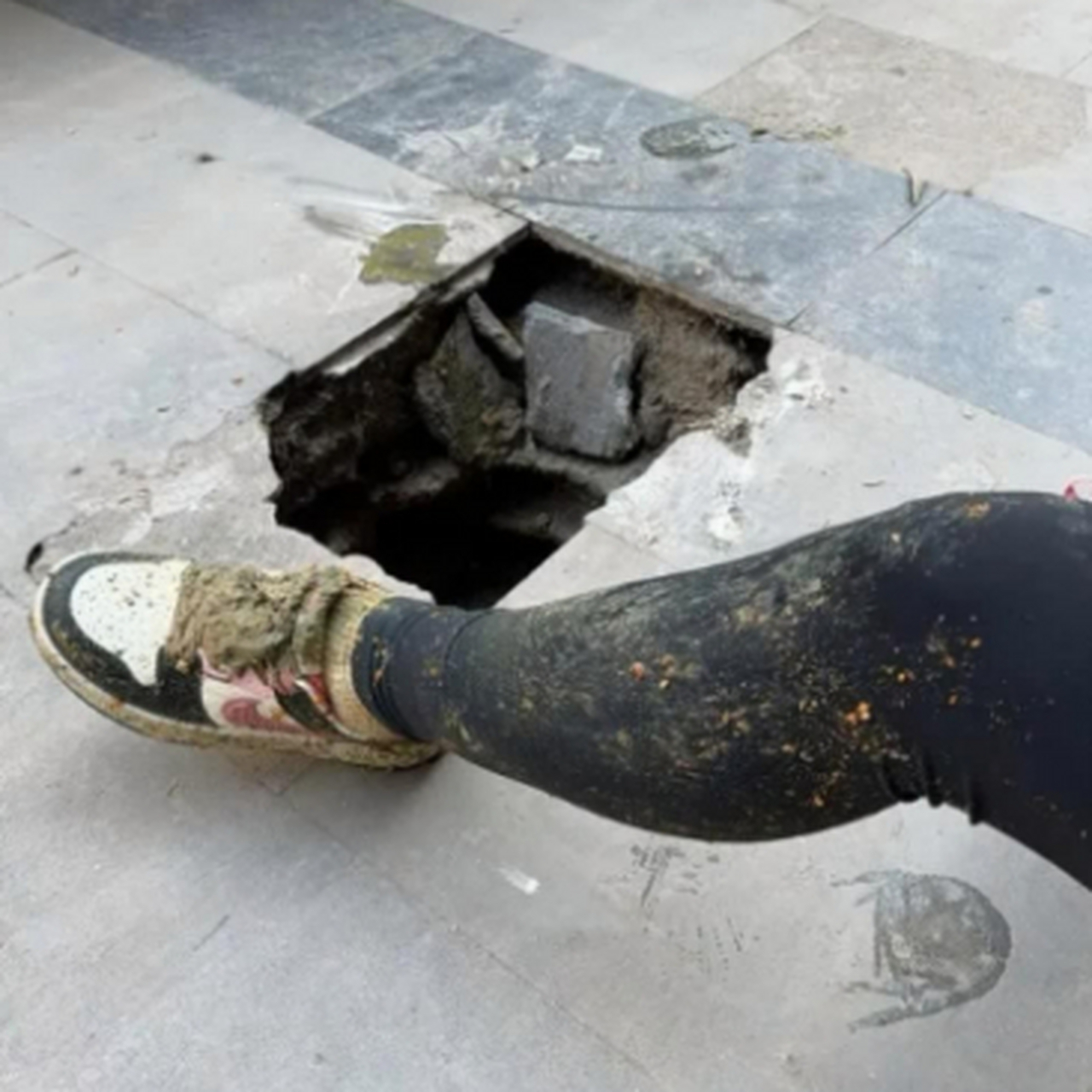 一女子行路时,一只脚突然踩进了路上塌陷的大坑里,鞋和腿粘了泥巴.