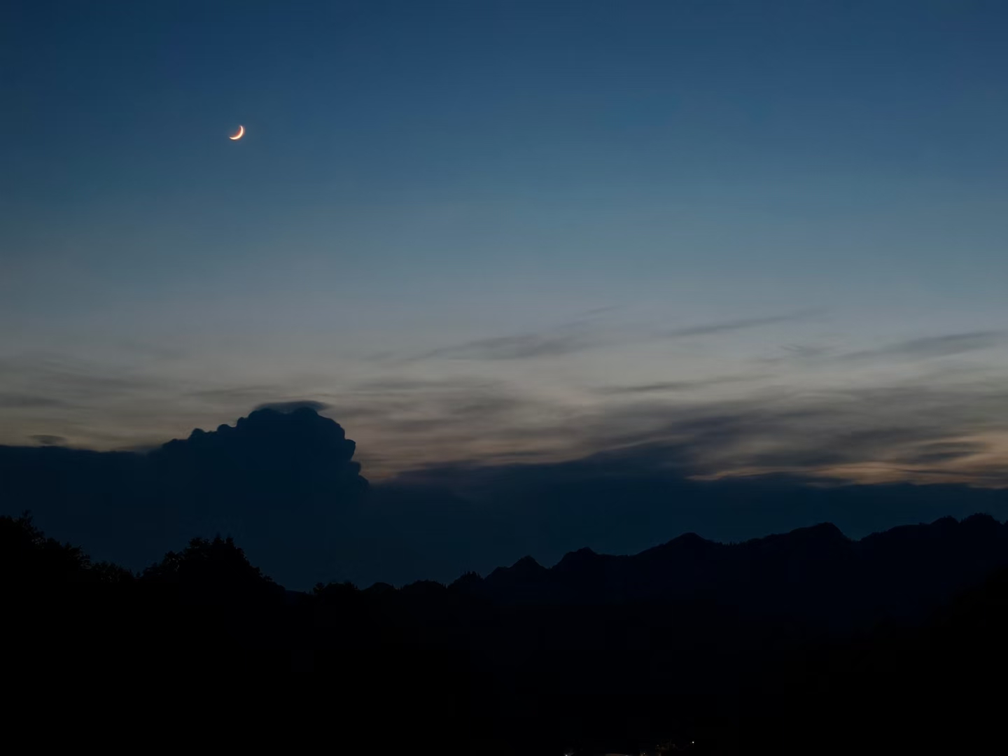 夜幕降临,月亮悄悄爬上天空,山峦的剪影在月光下更显深邃,云朵也变得