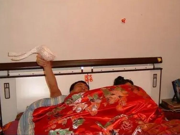 图片中,床上睡着一男一女,床头处仅见两个人头,盖着绸缎被面的被子像