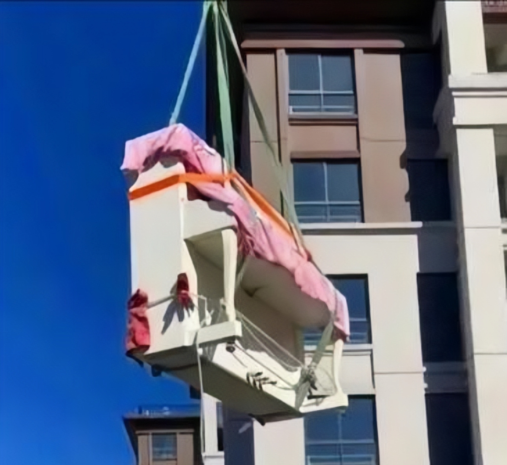 一台吊车正在把一架钢琴高高地吊起来,准备送进屋里,钢琴太大进不去