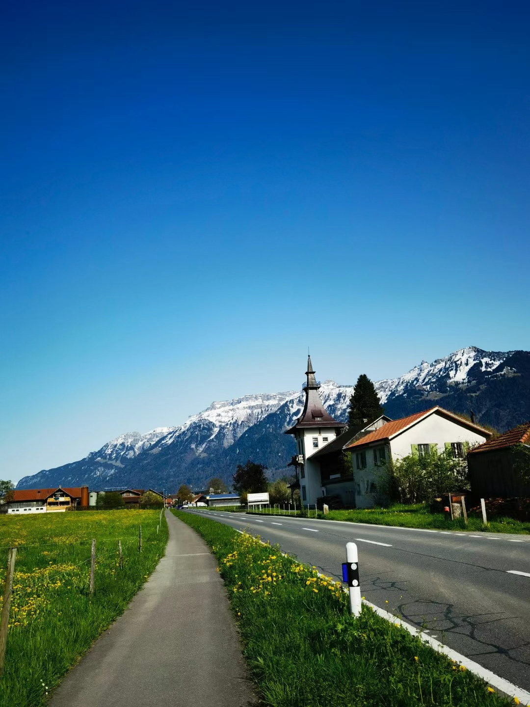 道路穿过碧绿的草地,两旁低矮房屋散落,远处的白色教堂在雪中静谧