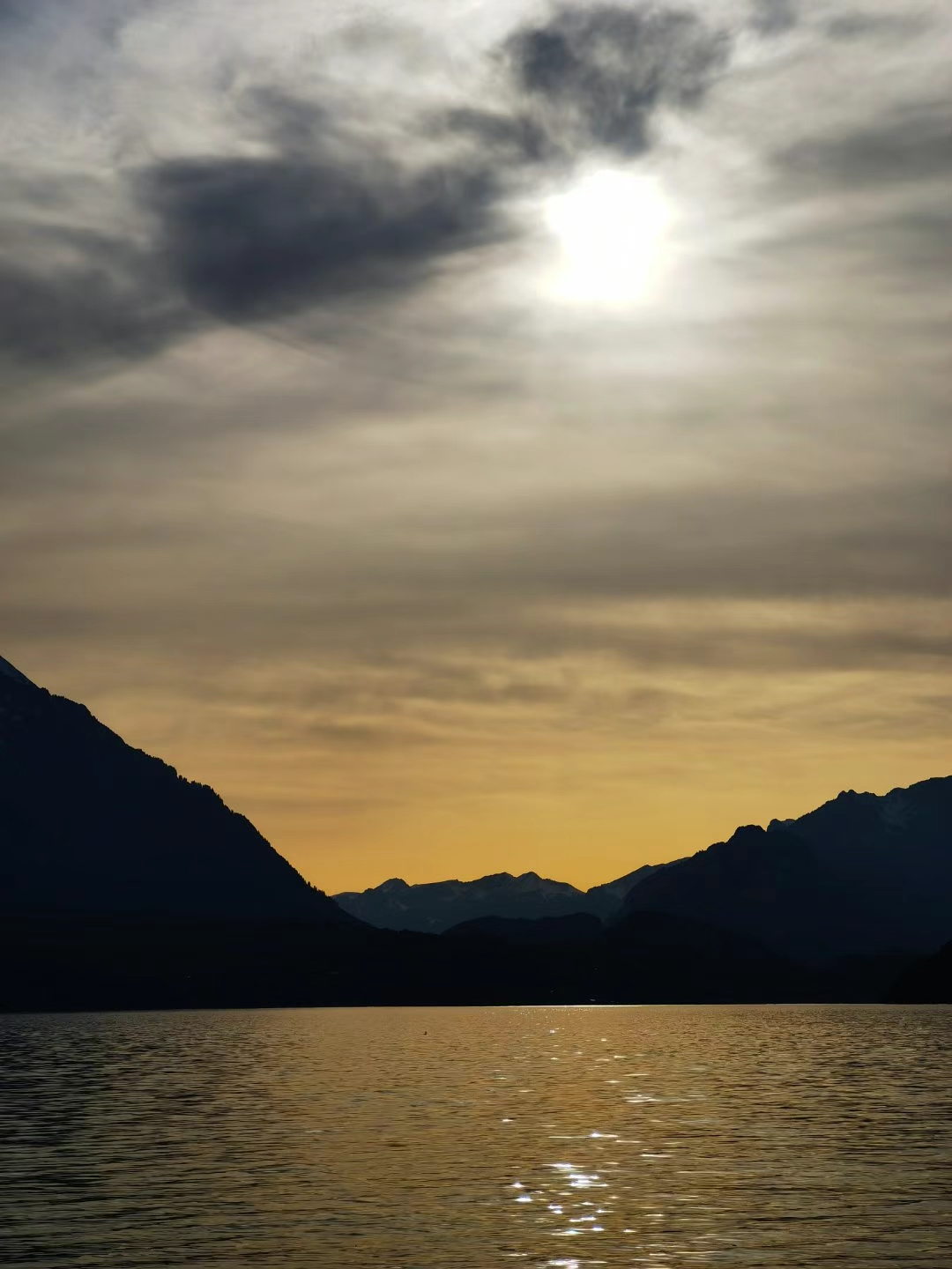 "夕阳余晖映湖面,天空渐变显神韵.远山如黛映金光,前景树木剪影深.