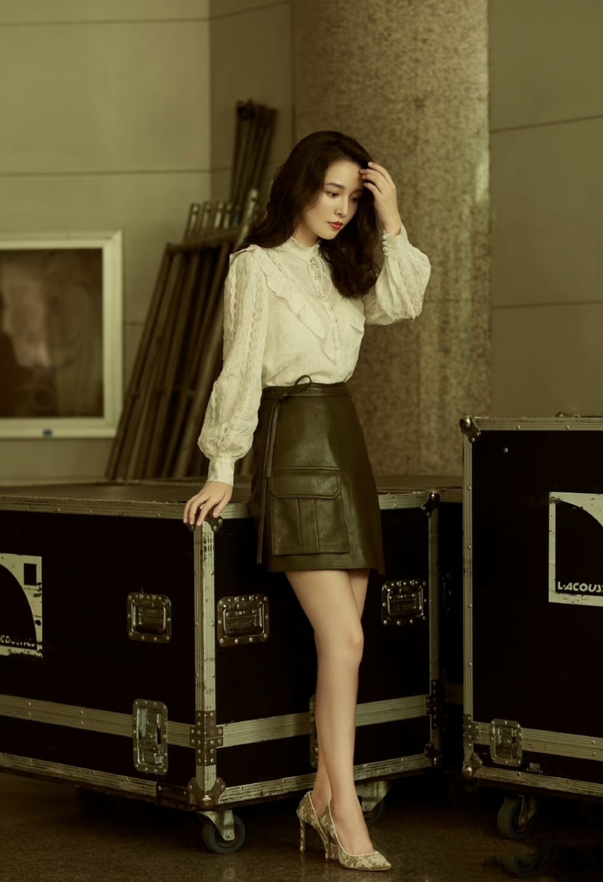 吴倩身穿白色荷叶衬衫搭配黑色皮裙和高跟鞋,蓬松的卷发搭配复古妆容