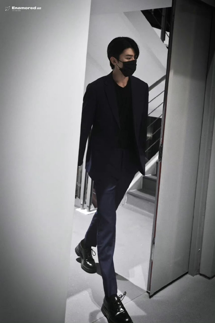 蔡徐坤身穿剪裁利落的暗夜蓝色西服套装搭配漆皮皮鞋,身姿挺拔,举手投