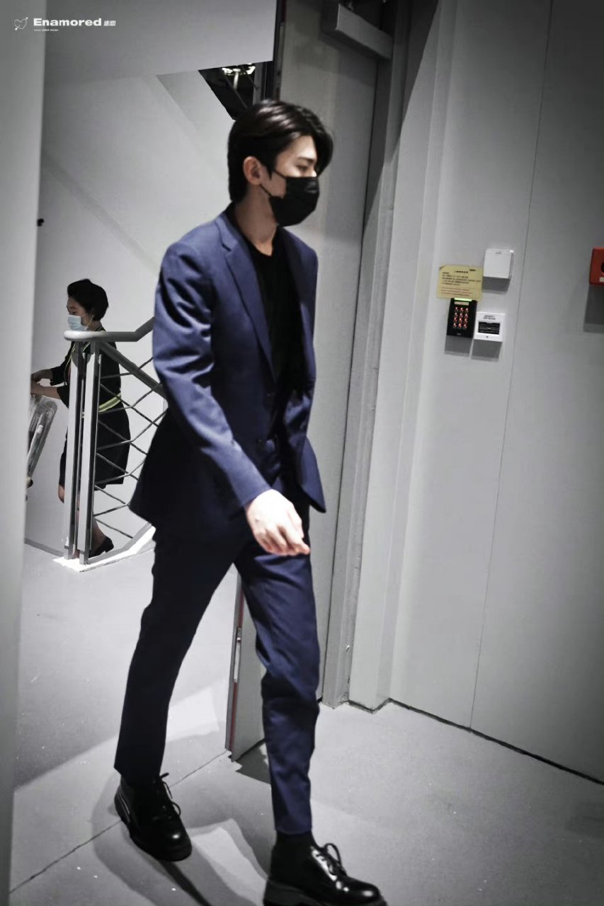 蔡徐坤身穿剪裁利落的暗夜蓝色西服套装搭配漆皮皮鞋,身姿挺拔,举手投