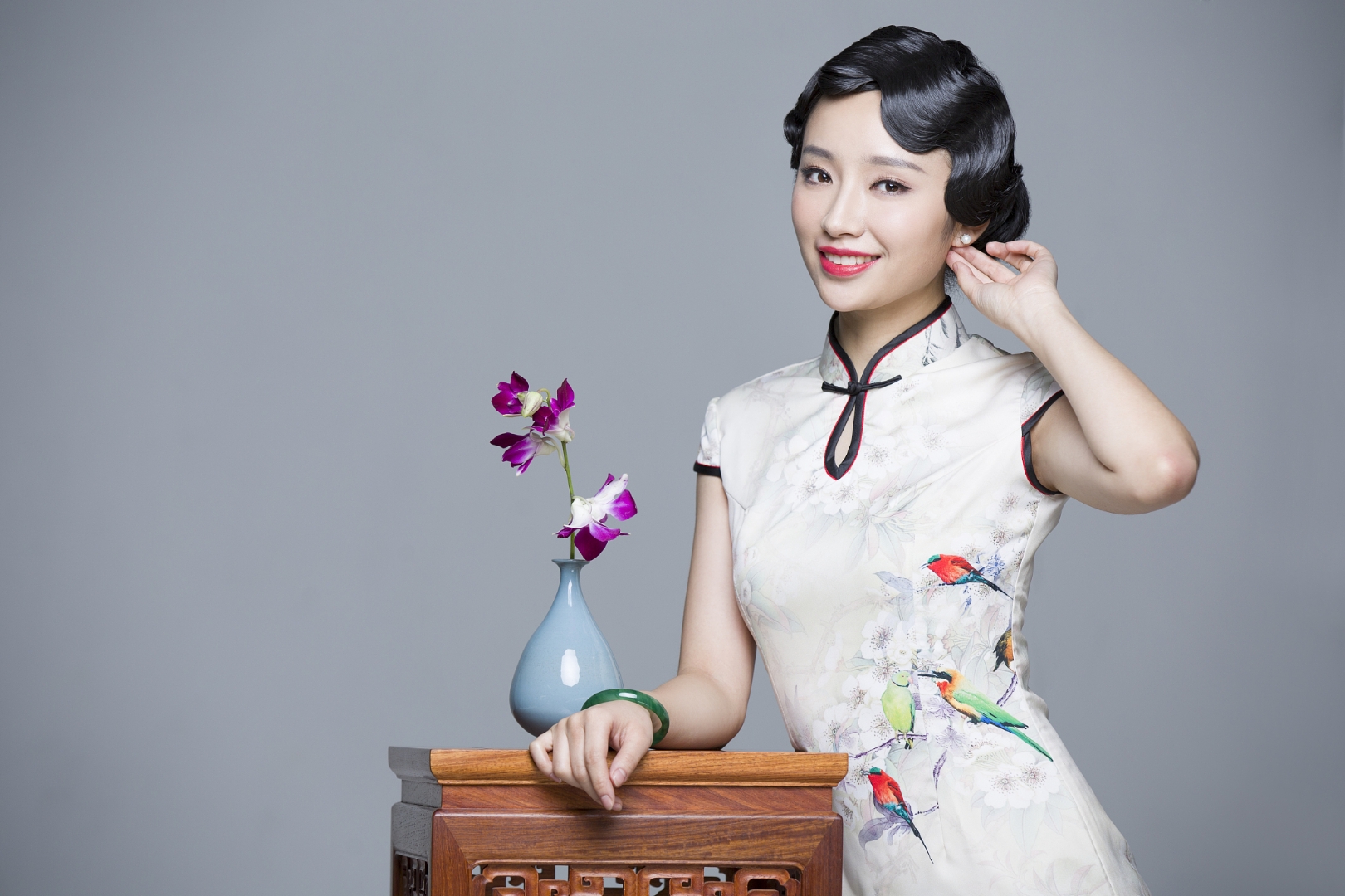 94这位穿着中国风服装的年轻女性,微笑着站在花瓶旁边,仿佛是一幅