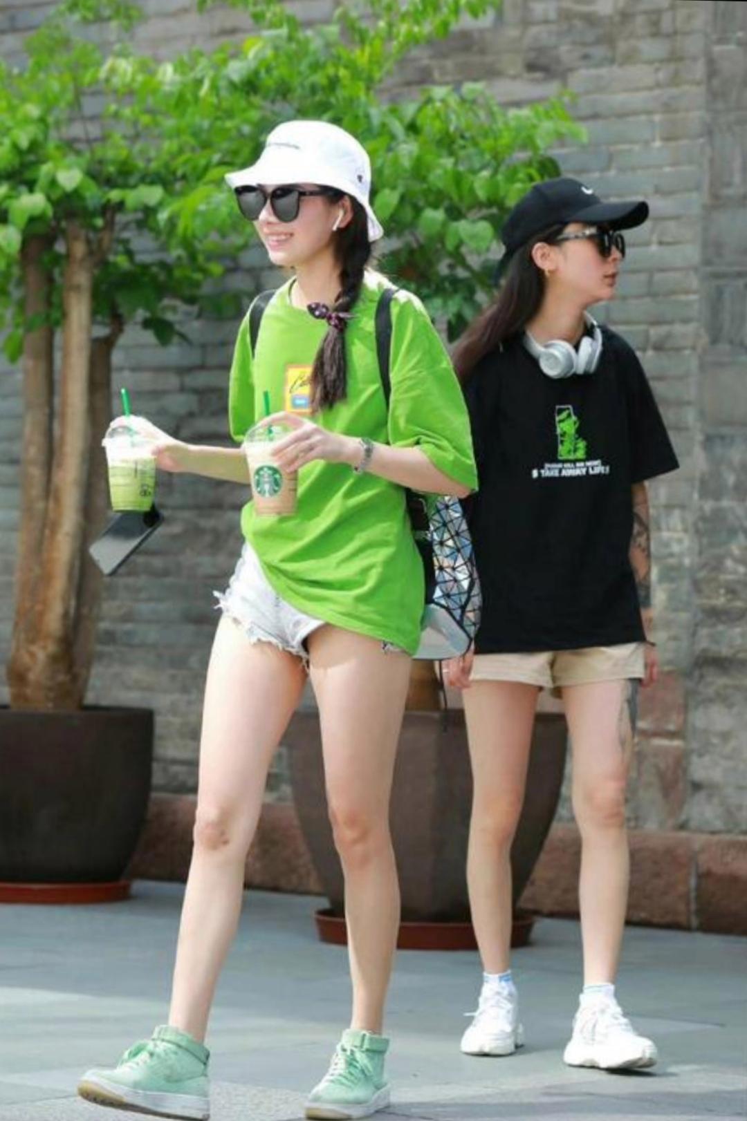 夏日街头,活力女孩绿色t恤搭配牛仔短裤,清爽时尚,一手拿着饮料,一手