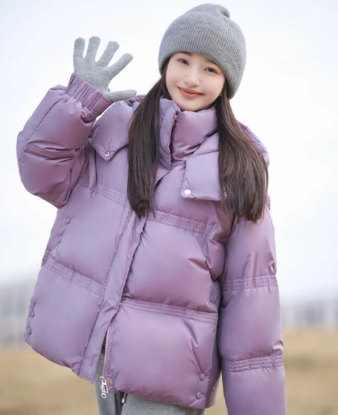 冬日里的小温暖,这个女孩穿着紫色羽绒服,戴着灰色帽子,蹲在树下微笑