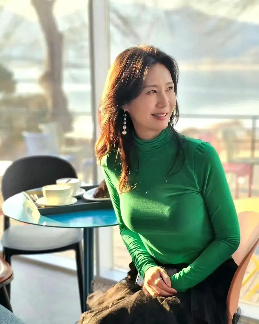 她,身穿鲜艳绿毛衣,佩戴长耳环,自然微笑,仿佛诉说