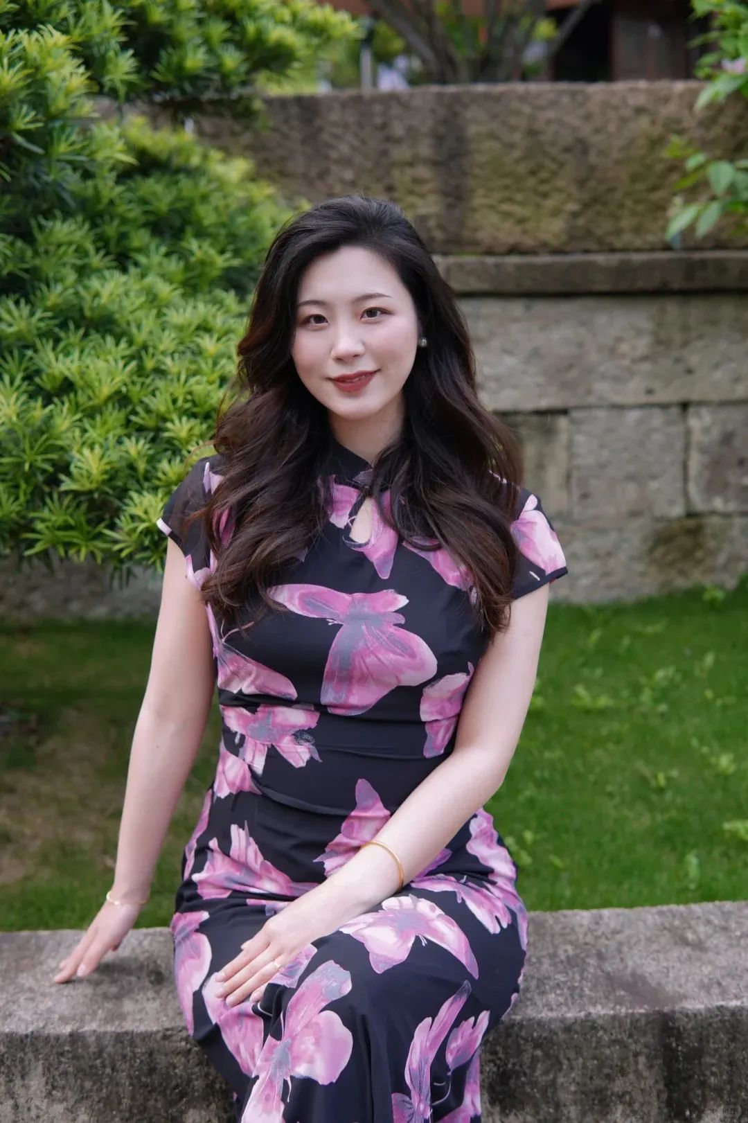 坐在石墙上,粉花旗袍美女,笑颜如花,美得不可方物