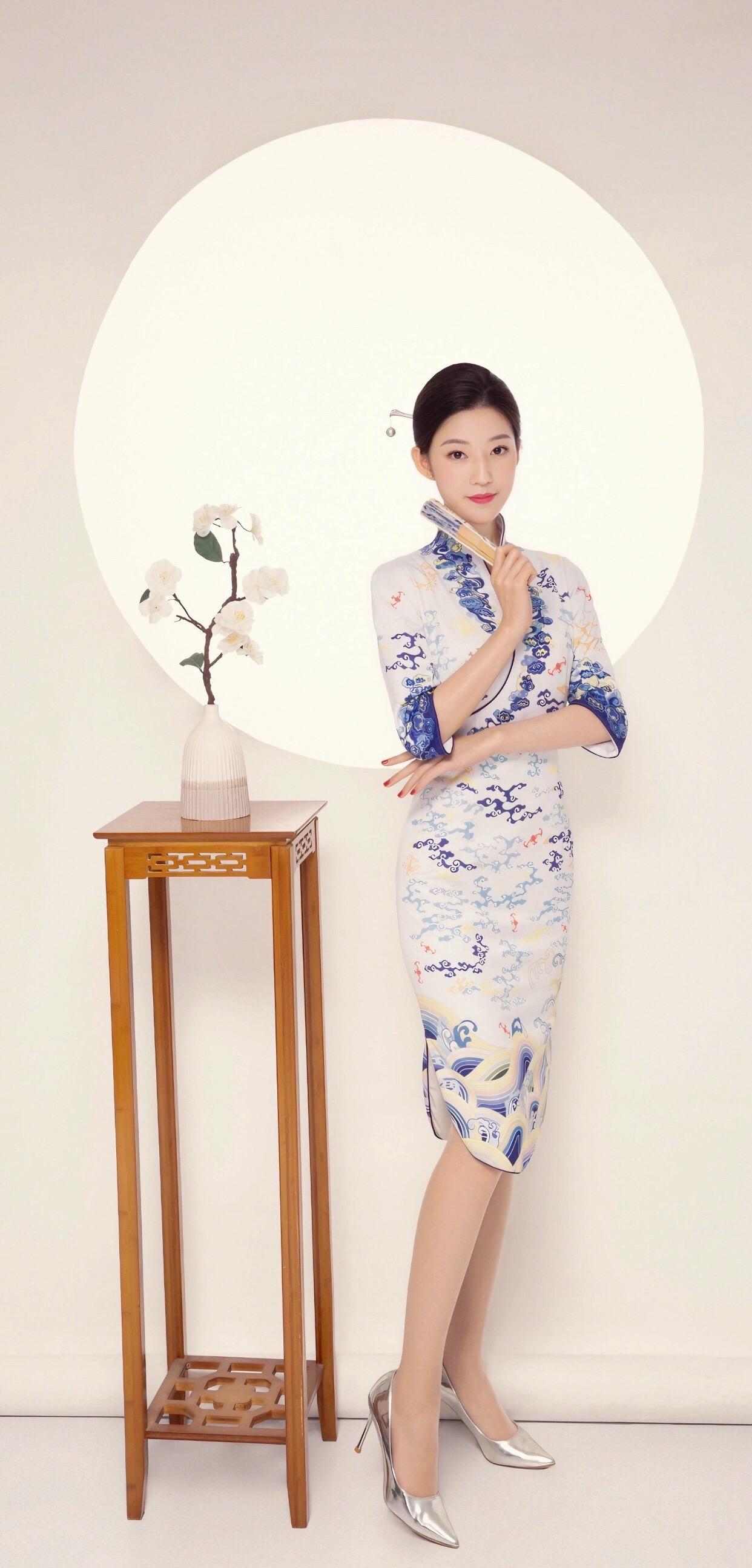 室内环境下,一位女子穿着蓝白相间的旗袍,红色的花朵犹如点缀在夜空中