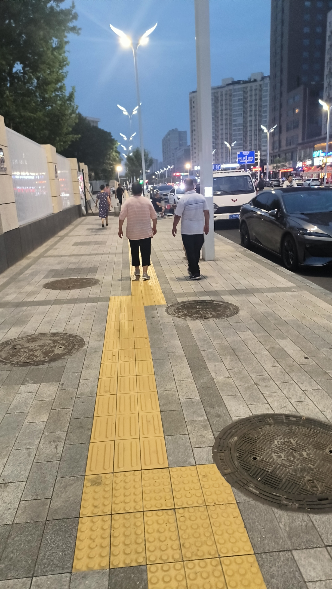 夜幕下的城市人行道,两个人悠闲地散步,周围是繁忙都市的缩影