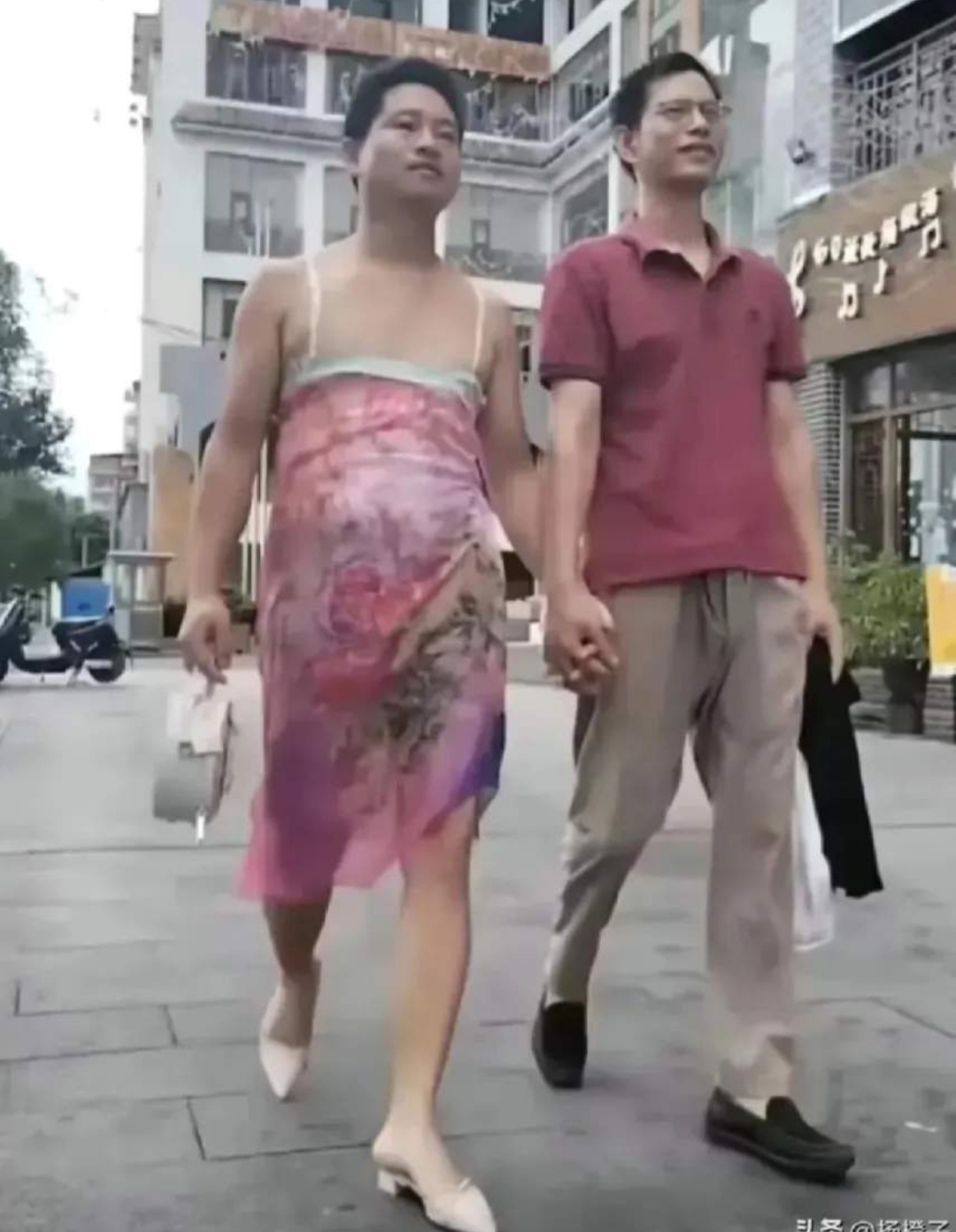 大小伙子穿花色鲜艳的吊带裙,穿高跟尖头的凉拖,与男士手拉手走在大街