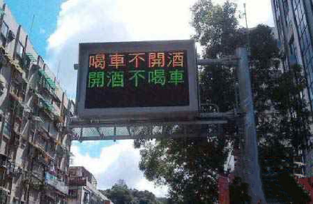 一条繁忙的街道旁立着一块黑色背景的交通警示牌,上面显示着黄色字和