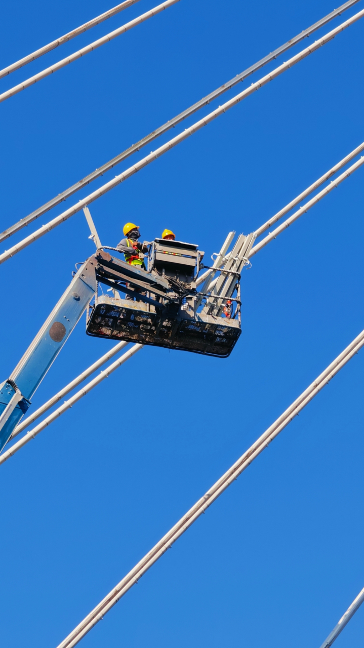 工人在高空作业车里,细心地维修着大桥拉索.