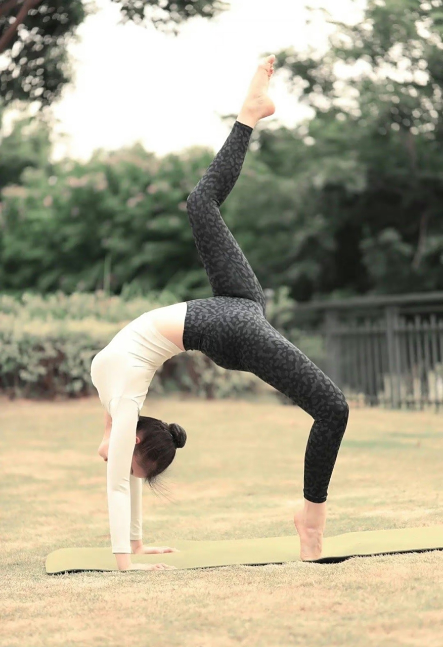 在翠绿的草坪上,一个年轻女性身着瑜伽服,展现着高难度的动作