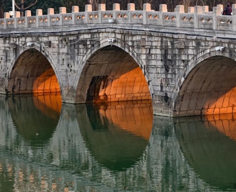 柔和的阳光透过拱形石桥,在饱经风霜的桥面上投下迷人的影子