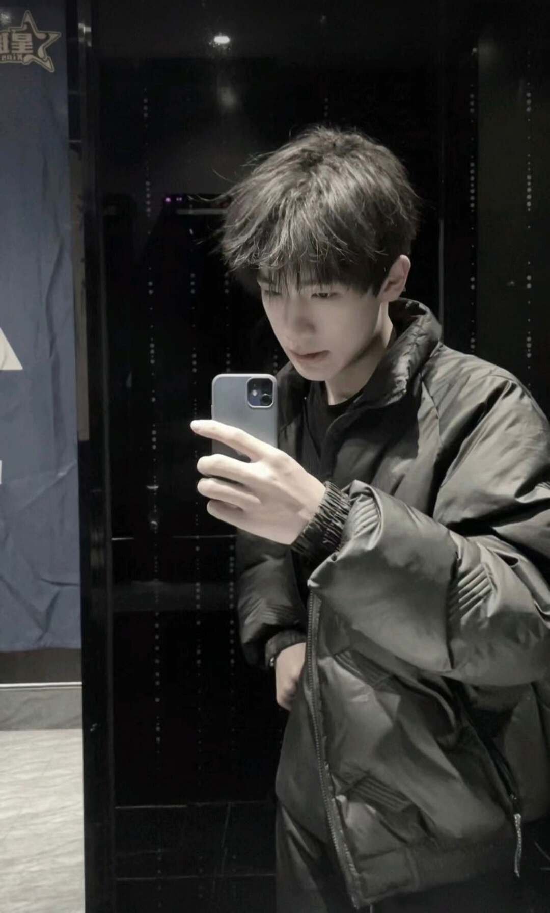 一位年轻男子,身着黑色外套,手持手机,眼中闪烁着对未来的无限憧憬与