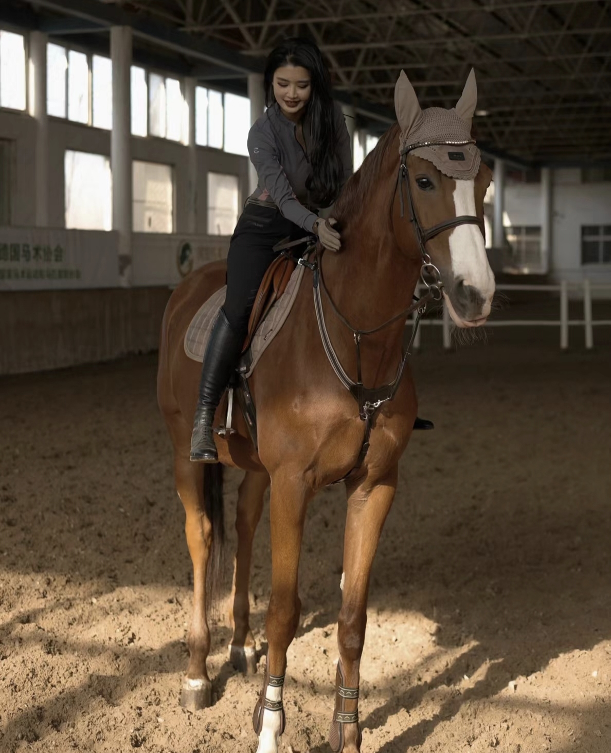 女子一身骑装,于身边棕褐色骏马亲密相依,身姿优雅,手轻抚马鬃,笑容