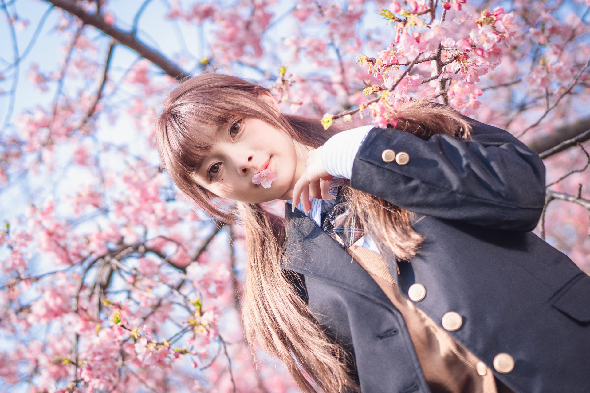 她一只手轻轻扶着樱花树,另一只手则向上张开,仿佛在与微风嬉戏,感受