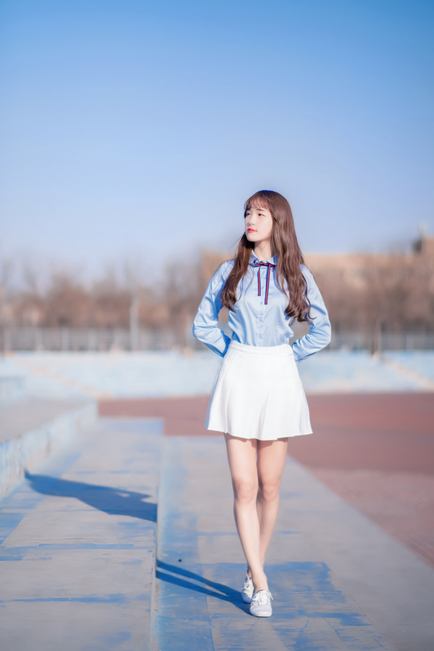 阳光下的自信女孩,穿着简约的蓝色衬衫和白色短裙,散发着迷人的气质.
