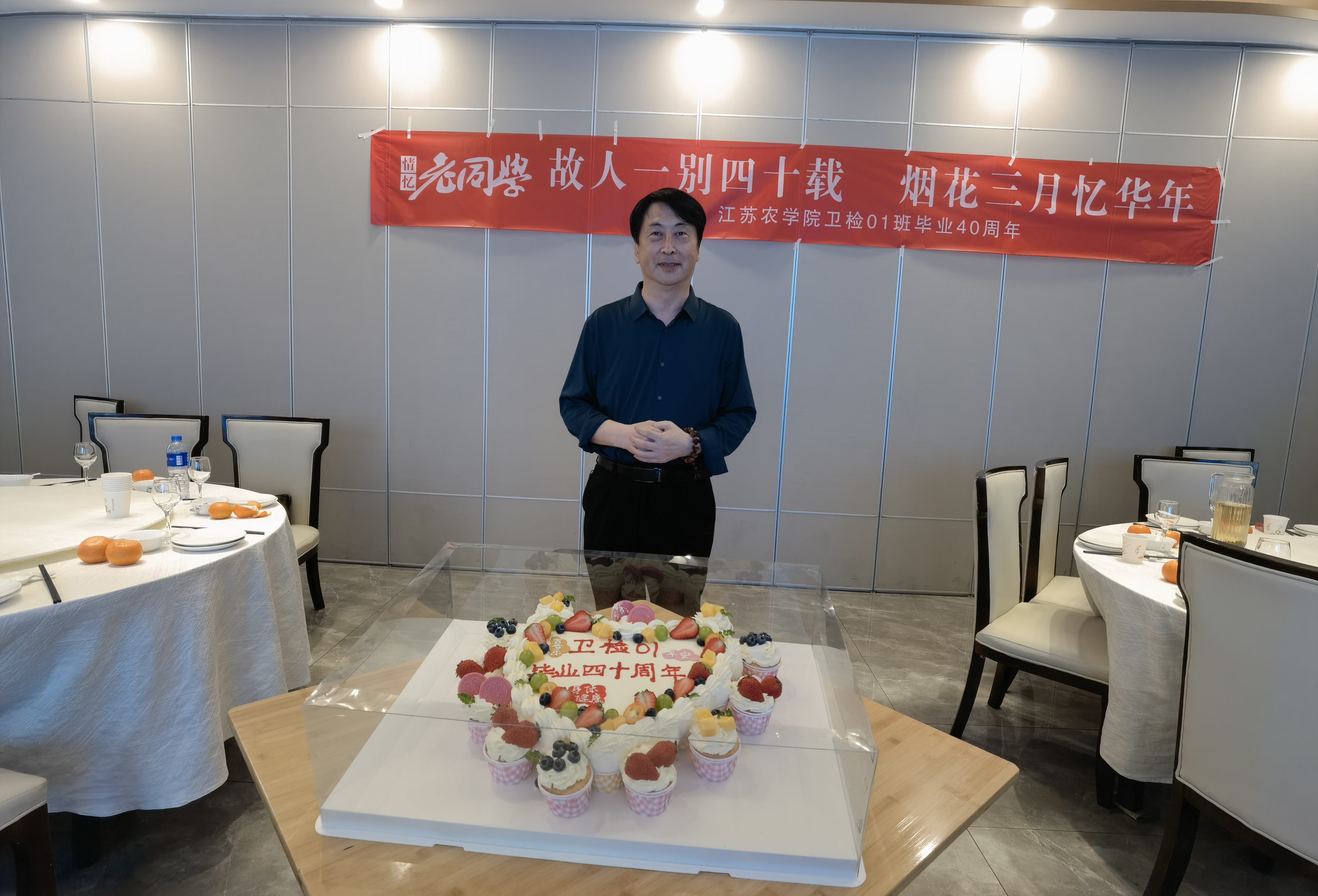 桌前他着深色衬衫,双手交叠,大型生日蛋糕庆四十大寿,水果环绕,红色