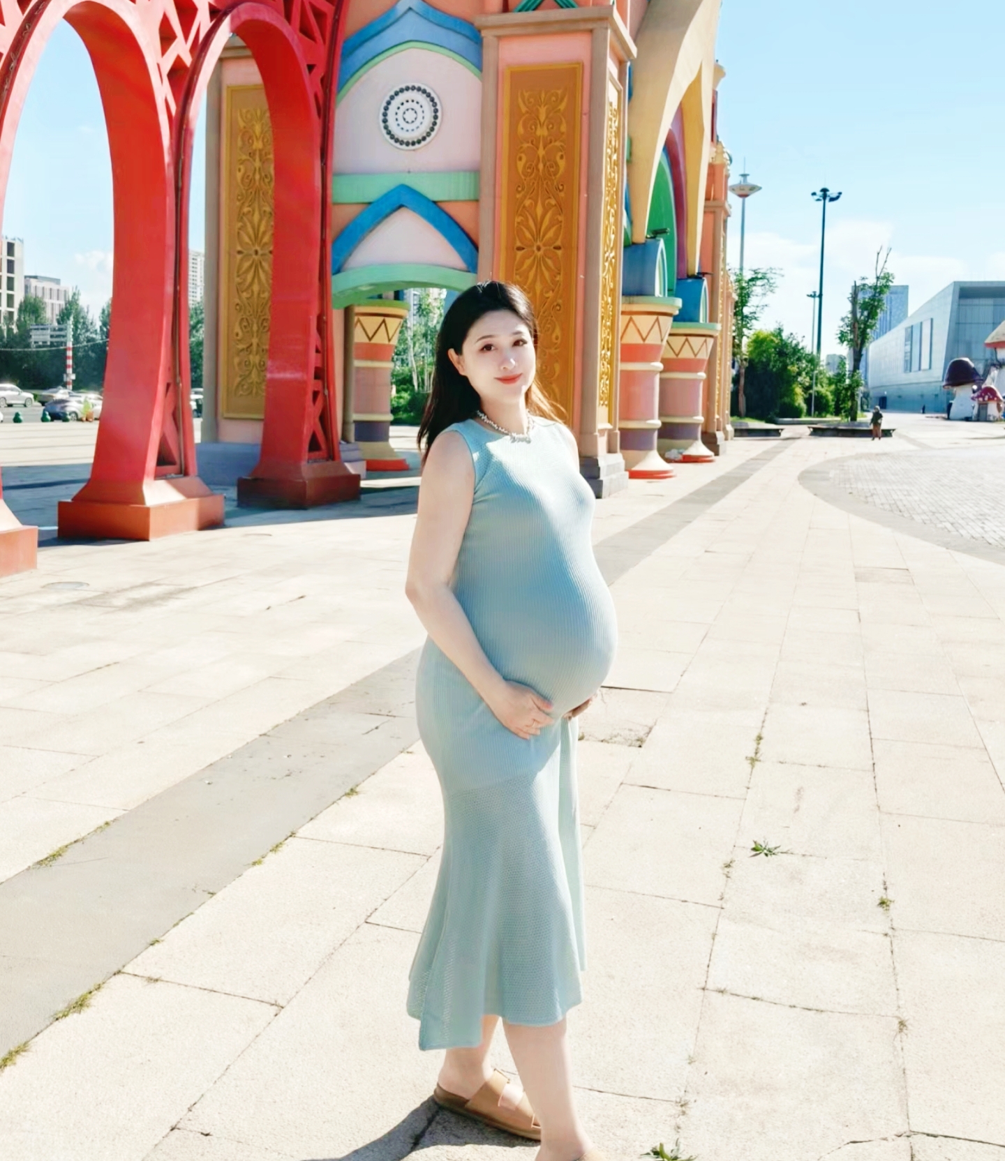 这个孕味十足的妈妈,站在漂亮的拱门前,充满喜悦的笑容,温柔地抚摸着