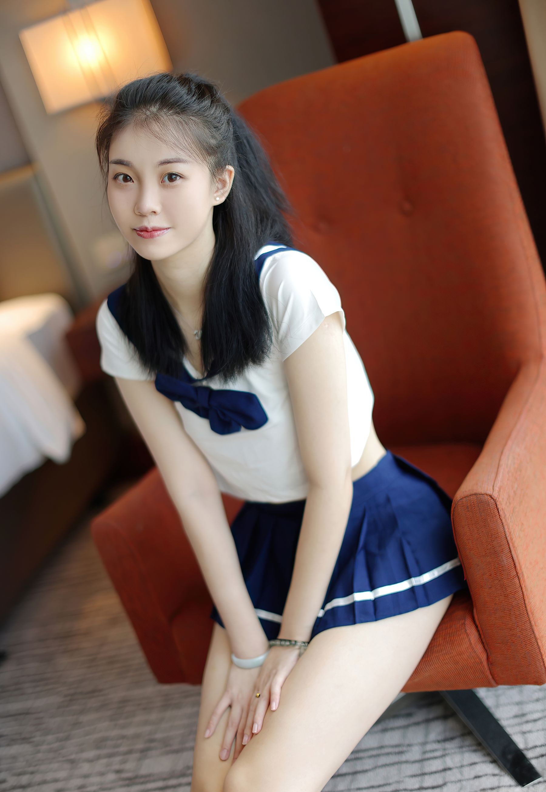 一位年轻的黑发女子坐在沙发上,身着经典的水手服,仿佛海风轻拂过脸颊