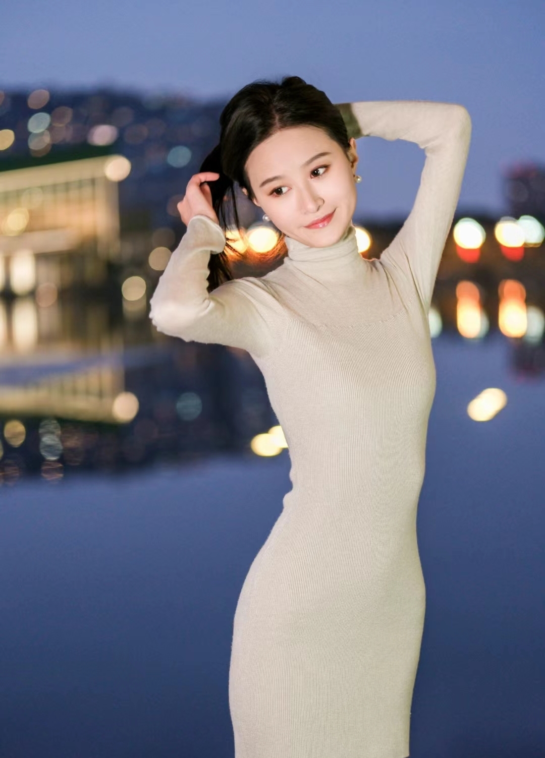 身着奶油色针织裙,散发着温婉气息,她站在城市夜景