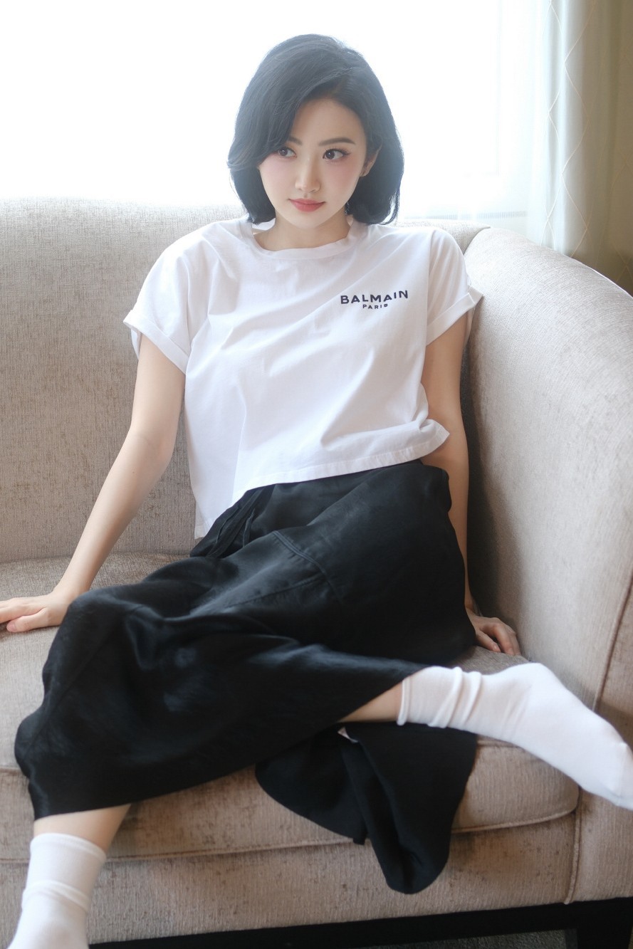 景甜坐在沙发上,腿交叉,白t恤配黑色裤裙,简约时尚,透露出一种随性的
