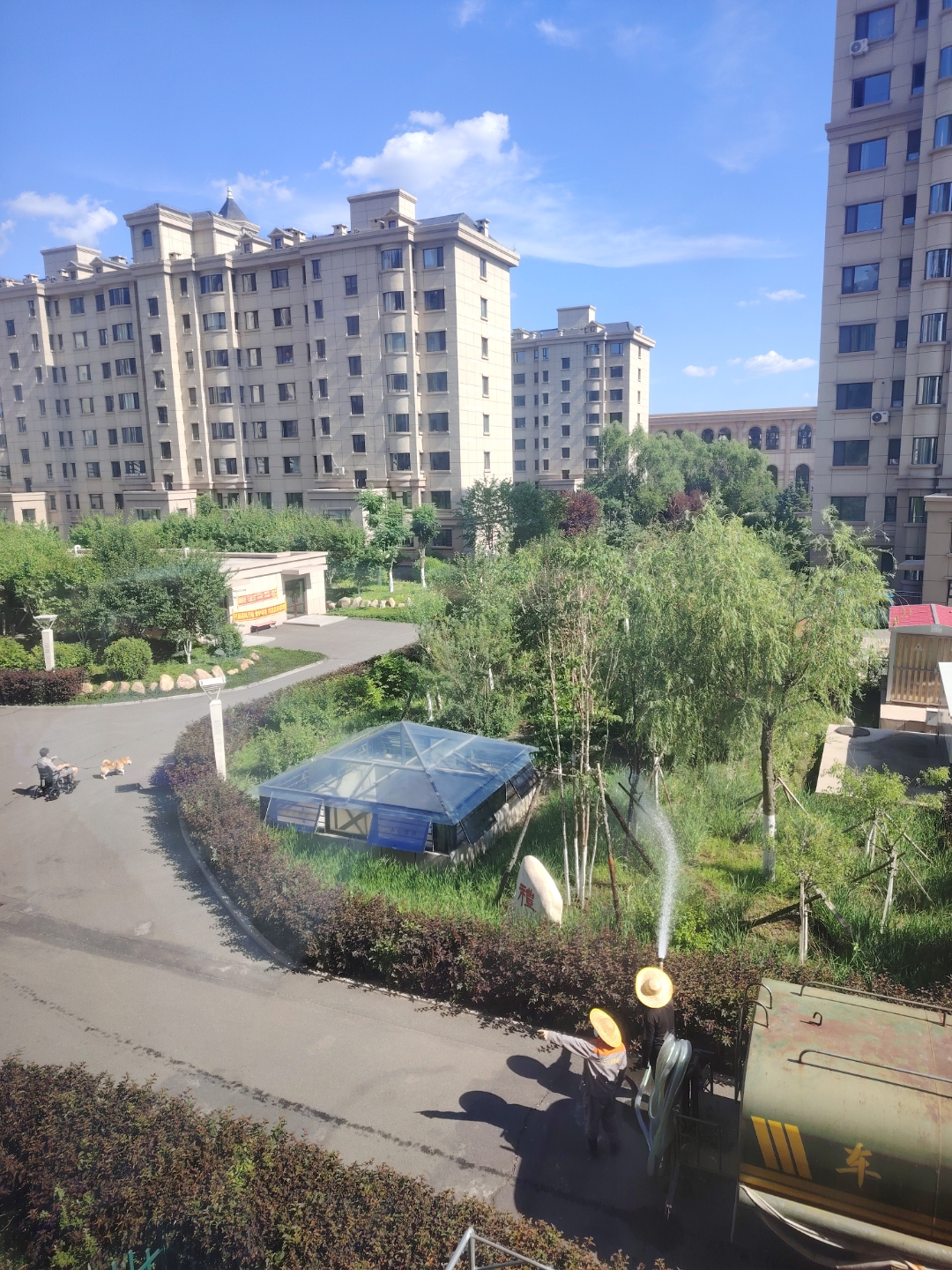 湛蓝的天空飘着几朵白云,物业人员正驾驶洒水车为绿植解渴