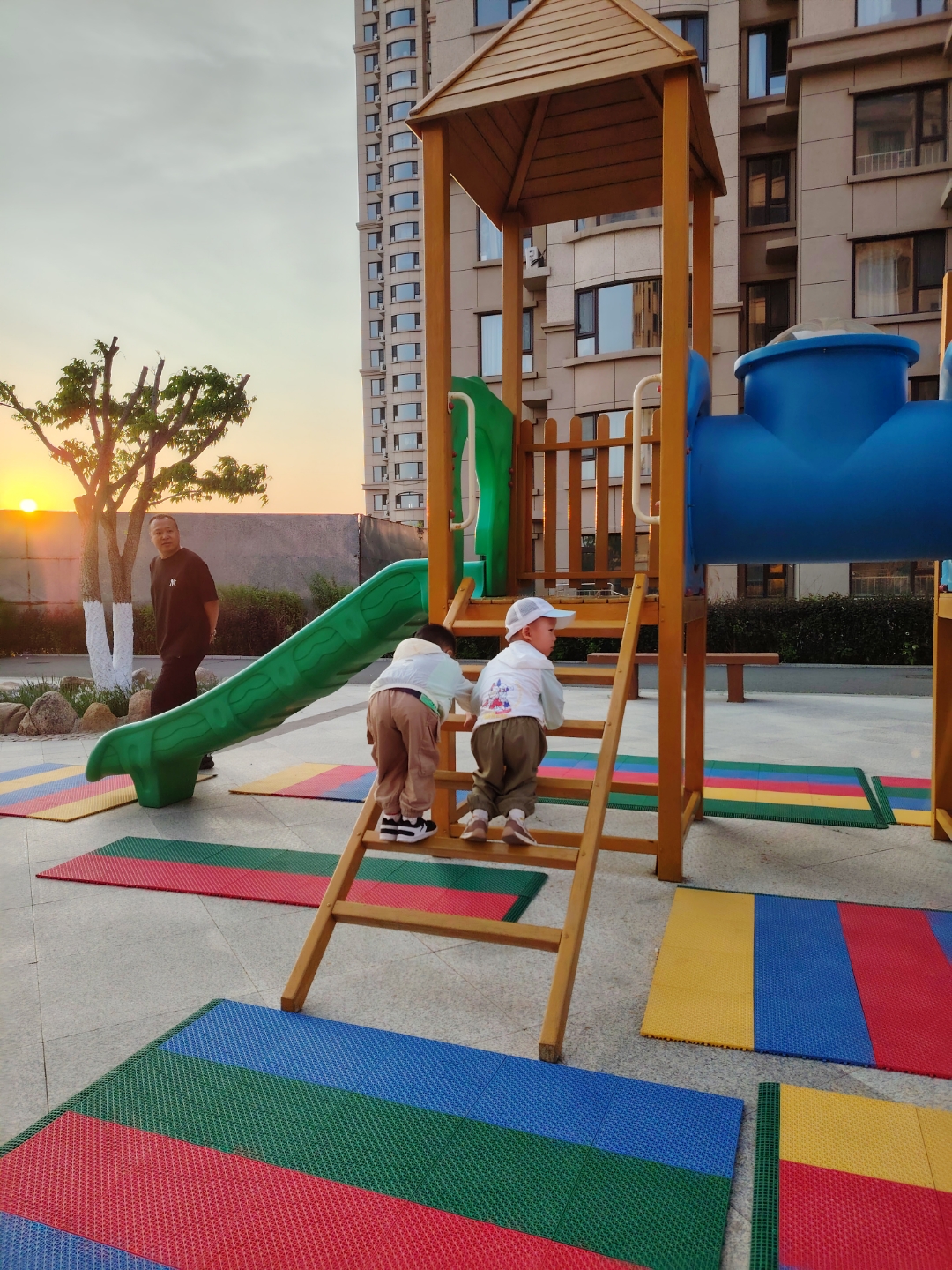 夕阳下,两个孩童在彩虹地砖上追逐嬉戏,清脆的笑声顺着滑梯溜进晚风里