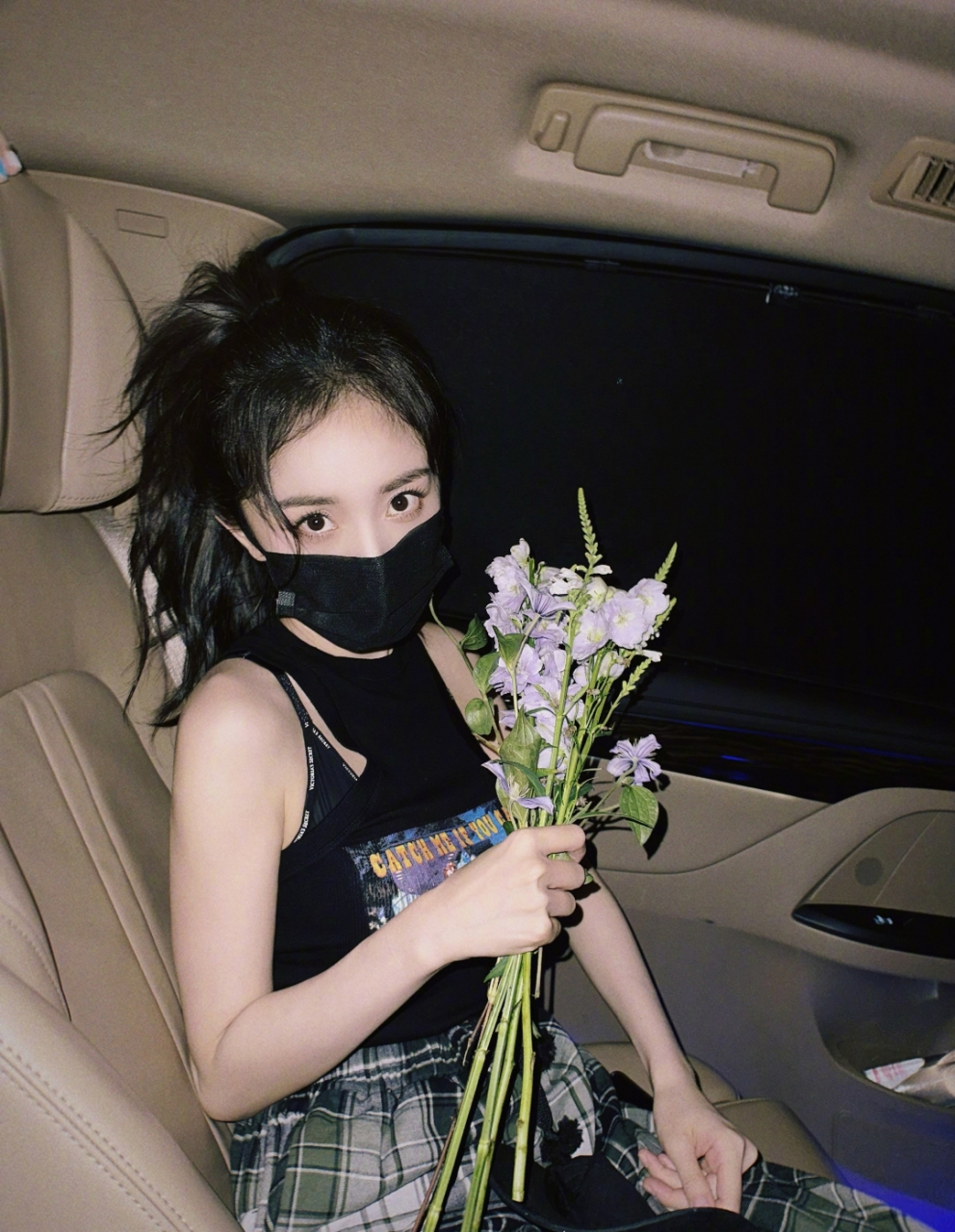 杨幂戴着黑口罩,手上还拿着花儿,坐在车里,依旧显得特别漂亮.