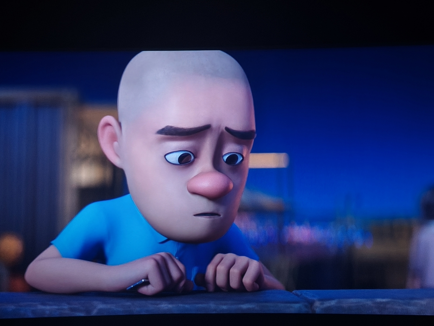 光头小男孩,身穿蓝色t恤,托着下巴,眼神专注.