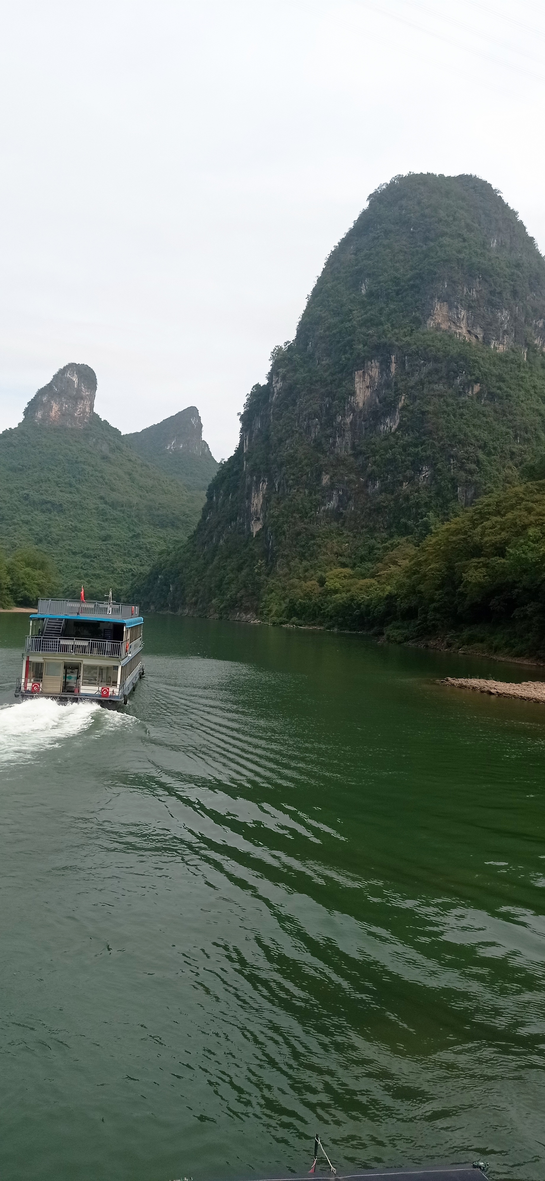 在一片如梦如幻的画卷中,一艘蓝色的游船在漓江上静静地行驶,船身随着