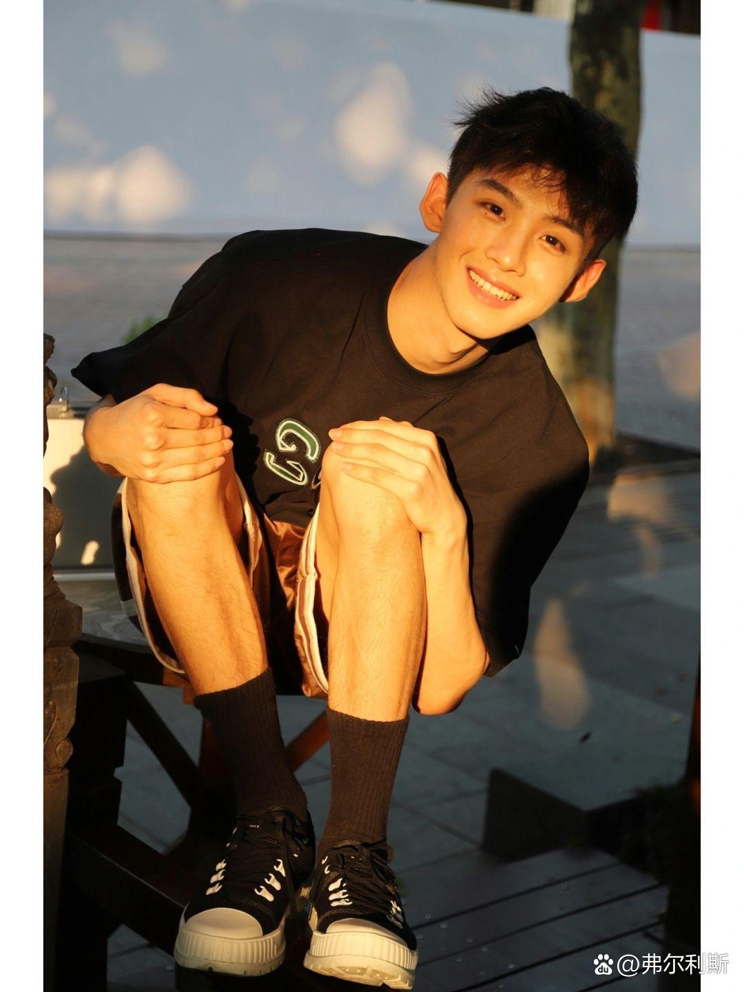 男孩身穿黑色t恤和短裤,简约又不失时尚感,蹲在那儿的他,阳光透过树叶