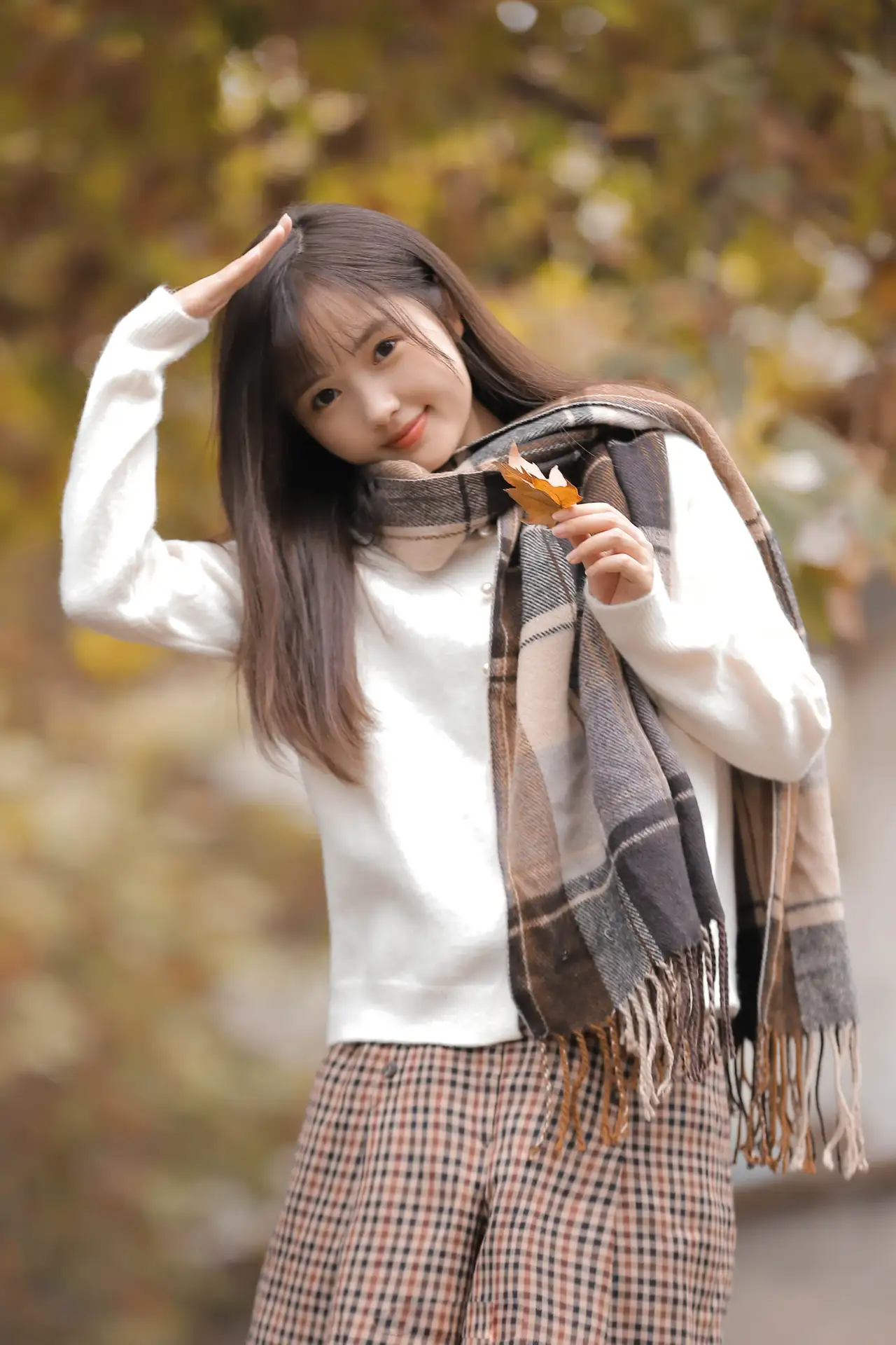 94身着白毛衣,围着格子围巾的长发少女,轻盈地站在木桥上.