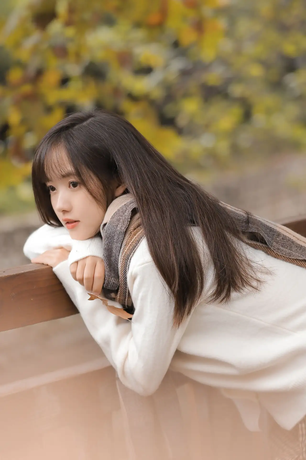 94身着白毛衣,围着格子围巾的长发少女,轻盈地站在木桥上.