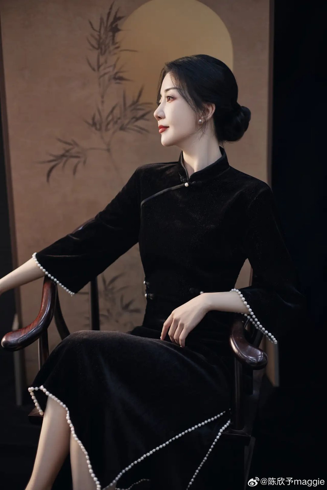 这组照片中,女子身穿黑色旗袍,端庄地坐在椅子上,她的黑发自然垂落