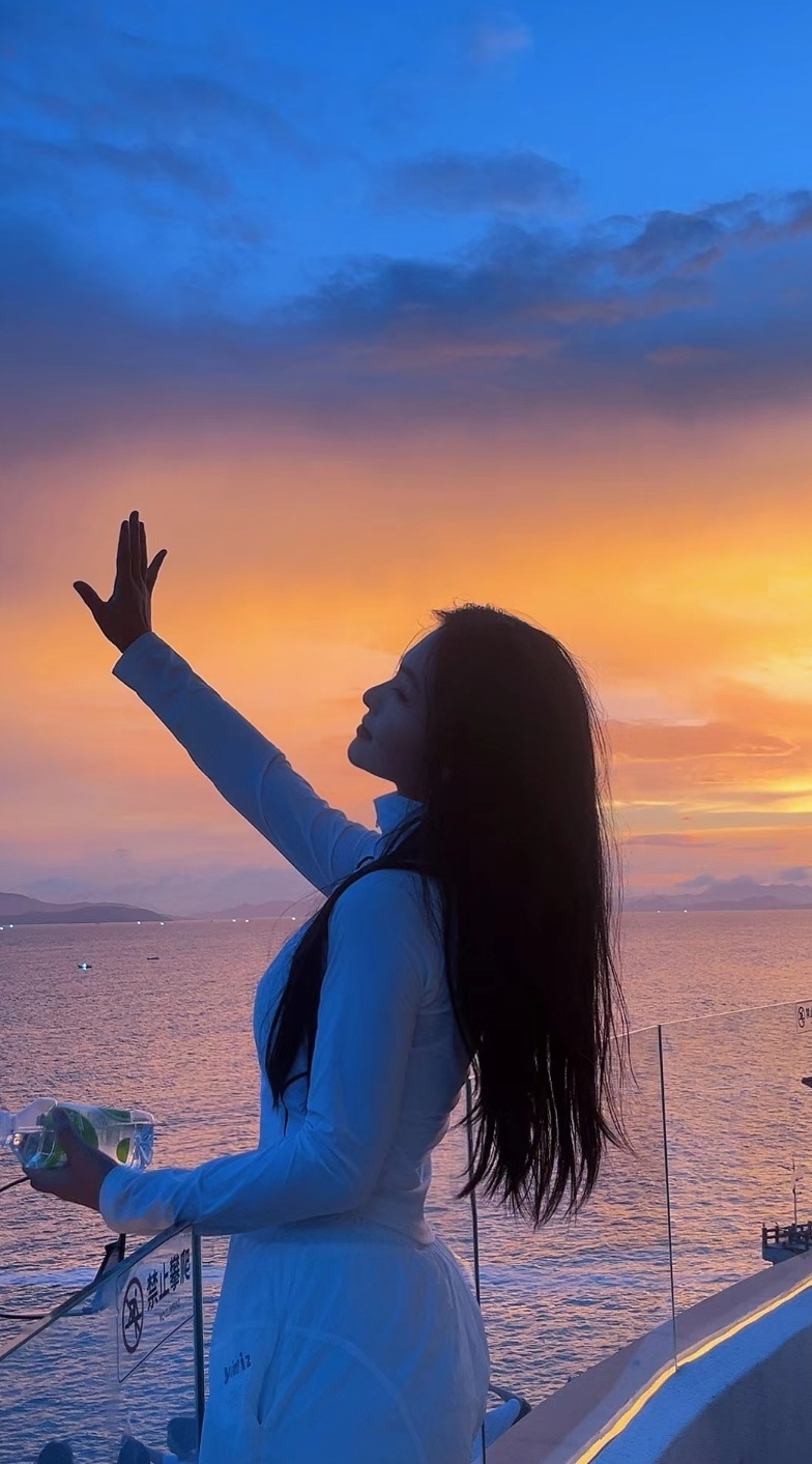 美女站在高台上,眺望远方.傍晚的海面,波光粼粼