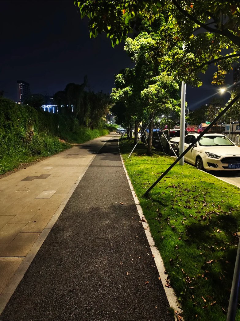 夜幕下的宁静小道,两旁绿树成荫,远处灯光闪烁,偶尔有车驶过,带来一丝