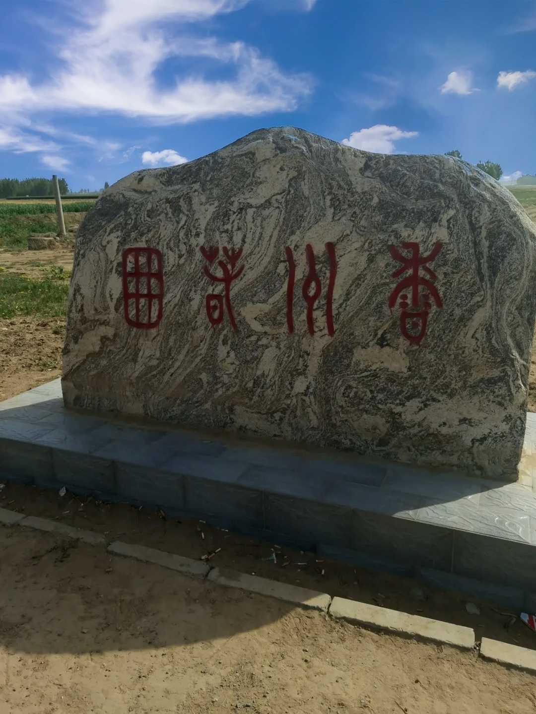 在蓝天白云的映衬下,一片开阔的田野中,一座花岗岩纪念碑静静矗立