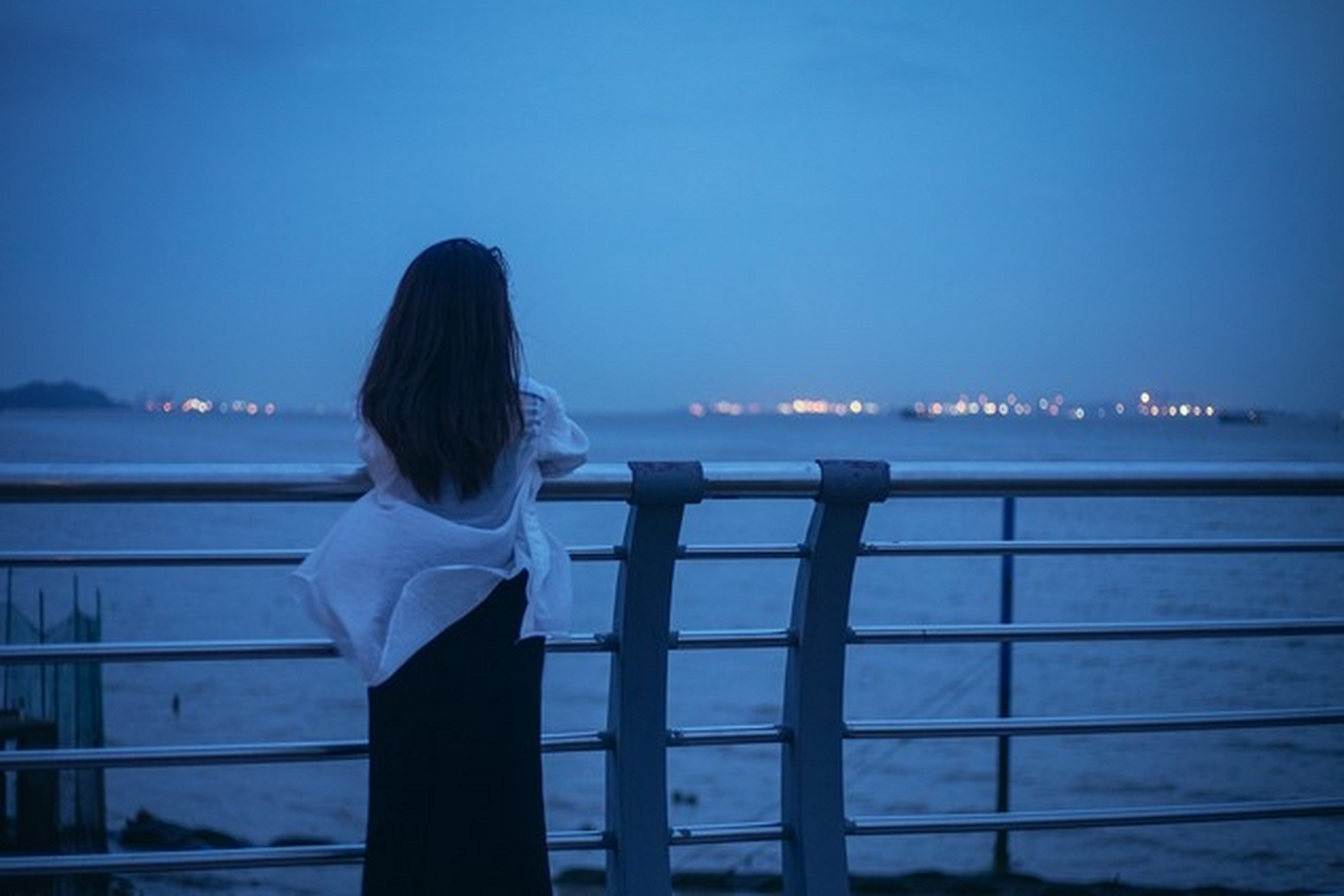 在夜幕降临的海边,她静静凝望着远方的城市灯火