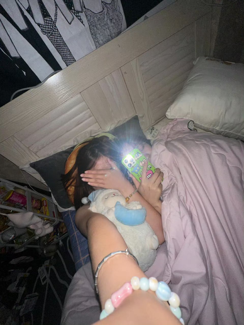 夜晚的卧室内,躺在床上,手拿手机,头戴发箍,粉色的床单,温馨而静谧.